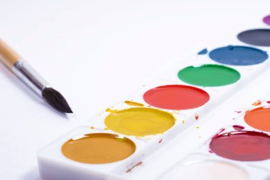 Renkli suluboya paleti, beyaz kağıt arka planda fırçalı boya fırçalarının üst görünümü