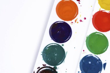 Renkli suluboya paleti, beyaz kağıt arka planda boya fırçalarının üst görünümü