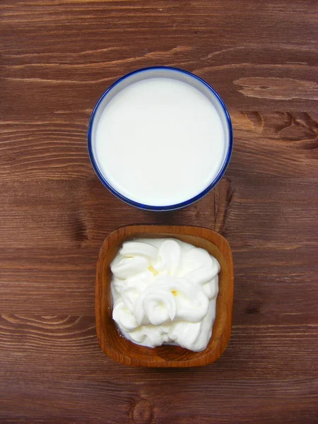 牛奶和酸奶油在木碗木桌垂直平的看法 — 图库照片