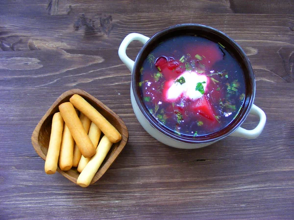 Closeup of russian traditional borscht, flat view with batons of bread on wooden brown background