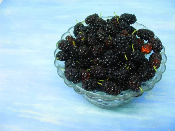 Fresh black mulberry in crystal bowl on blue shabby table