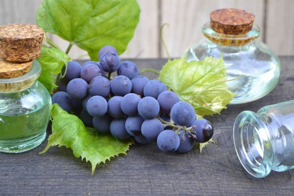 Grape seed oil in little bottles with blue grape on rustic dark wooden table