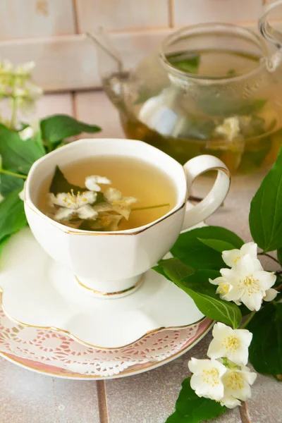 Jasmine tea with jasmine flowers on white wooden table background. Cup of hot green tea with jasmine flavor, fresh jasmine flowers. Concept of freshly drink.