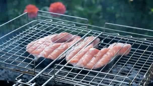 La main des hommes retourne le poisson dans le treillis sur le barbecue. Style de vie du village. Poisson rouge saumon sur un gril. Griller les steaks de truite — Video