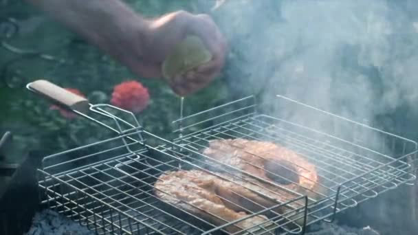 Mano humana exprimiendo jugo de lima en el pescado en la rejilla en la barbacoa. Pescado rojo salmón en una parrilla. Asar filetes de trucha. Chef exprime un limón medio cortado sobre el pescado — Vídeo de stock