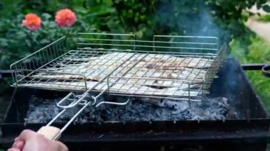  Çelenk. Erkeklerin eli barbeküdeki balık kafesini çeviriyor. Köyün yaşam tarzı. Izgaradaki Belone Belone. Izgara. Açık ateşte kızartılmış balık pişirmek. Barbekü, dışarıda. 