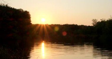 Nehir kenarındaki doğada kamp yapmak. Göl kenarında sakin bir akşam, yanan altın gökyüzü. Ormandaki deniz kıyısında renkli günbatımı gökyüzü. Ağaçların silueti ve arkasında büyük turuncu bir güneş