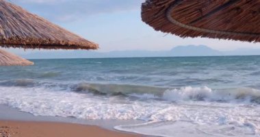 Deniz manzarası ve sazdan yapılmış şemsiyeler arasında tropik deniz manzarası. Kristal berrak turkuaz denizin arka planında boş kumlu bir sahil. Tatil kavramı