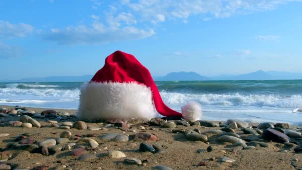 穏やかな波と熱帯の砂浜でクリスマスサンタクロースの帽子。冬休みだ島での新年のお祝い。コンセプト — ストック動画