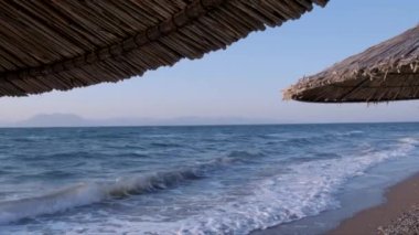  Deniz manzarası ve sazdan yapılmış şemsiyeler arasında tropik deniz manzarası. Kristal berrak turkuaz denizin arka planında boş kumlu bir sahil. Tatil kavramı