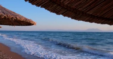 Deniz manzarası ve sazdan yapılmış şemsiyeler arasında tropik deniz manzarası. Kristal berrak turkuaz denizin arka planında boş kumlu bir sahil. Tatil kavramı