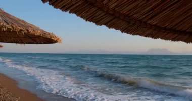Deniz manzarası ve sazdan yapılmış şemsiyeler arasında tropik deniz manzarası. Kristal berrak turkuaz denizin arka planında boş kumlu bir sahil. Tatil kavramı
