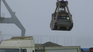 Nehir limanında gemiden kamyona beton döken vinç. Tozlu kargoların mavna teslimatı. Limanda, açık havada Gantry vinci boşaltılıp yükleniyor. Lojistik. Ticaret, denizcilik.