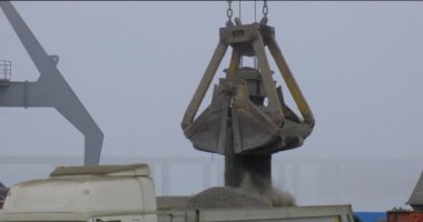 Nehir limanında gemiden kamyona beton döken vinç. Tozlu kargoların mavna teslimatı. Limanda, açık havada Gantry vinci boşaltılıp yükleniyor. Lojistik. Ticaret, denizcilik.