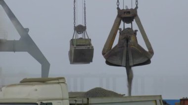 Nehir limanında gemiden kamyona beton döken vinç. Tozlu kargoların mavna teslimatı. Limanda, açık havada Gantry vinci boşaltılıp yükleniyor. Lojistik. Ticaret, denizcilik.