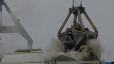 Nehir limanında gemiden kamyona beton döken vinç. Tozlu kargoların mavna teslimatı. Limanda, açık havada Gantry vinci boşaltılıp yükleniyor. Lojistik. Ticaret, denizcilik.