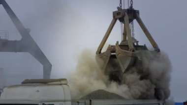 Nehir limanında gemiden kamyona beton döken vinç. Tozlu kargoların mavna teslimatı. Limanda, açık havada Gantry vinci boşaltılıp yükleniyor. Lojistik. Ticaret, denizcilik.