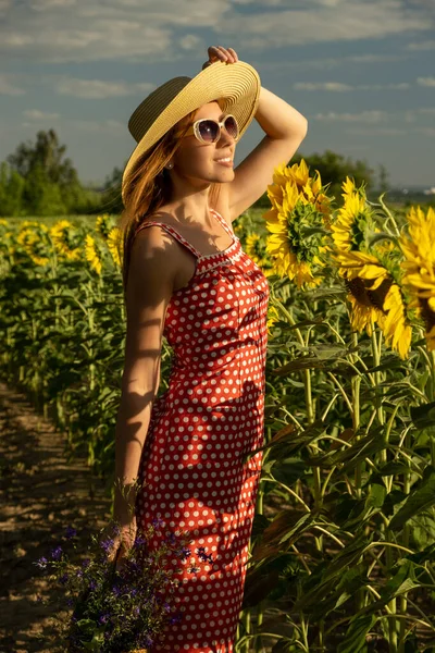 夏の日に一人でひまわり畑を歩いている女性 藁帽子と赤い水玉のドレスの美しい女の子は 田舎の風景を旅し 通過します 幸せな人間の屋外 — ストック写真