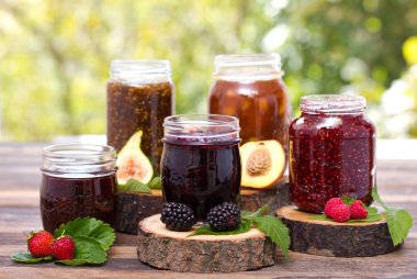 close up view of homemade jams in glass jars on wooden background clipart