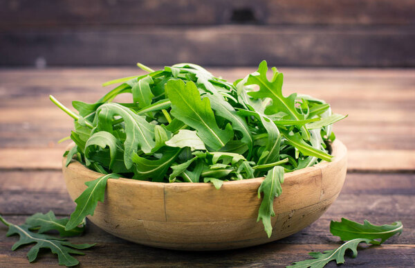 close up view of fresh arugula in bowl on wooden table