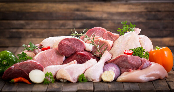 close up view of assorted raw meat with vegetables on wooden background