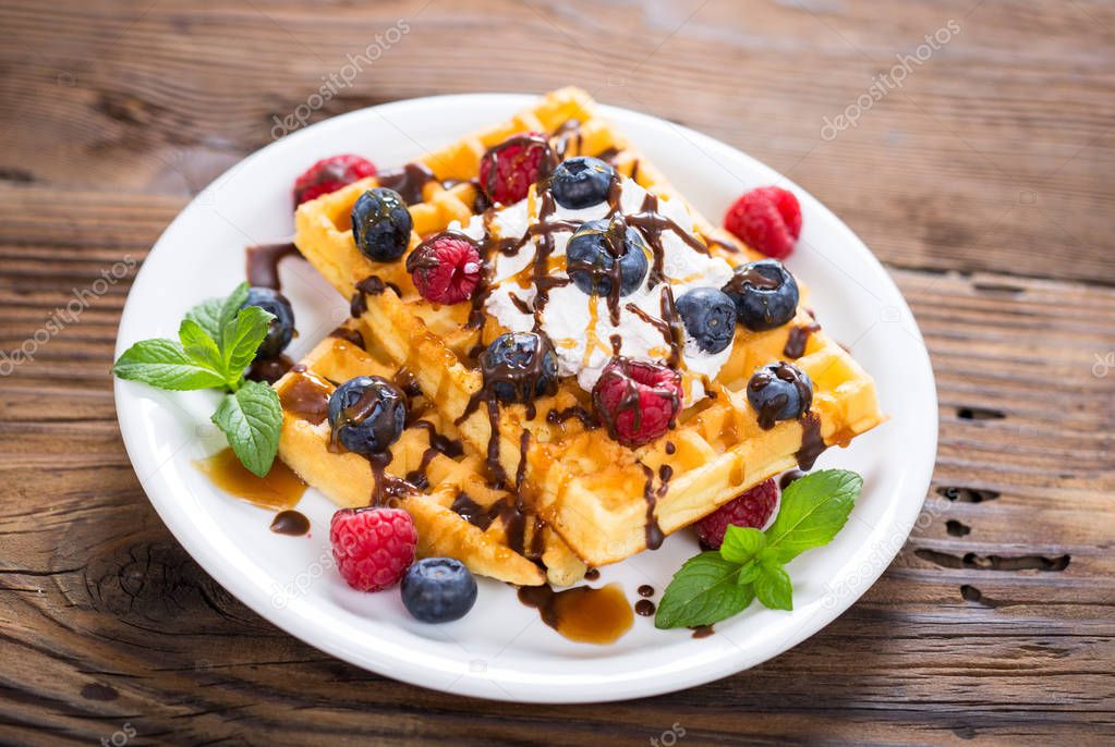 sweet waffles with chocolate and berries on wooden backdrop
