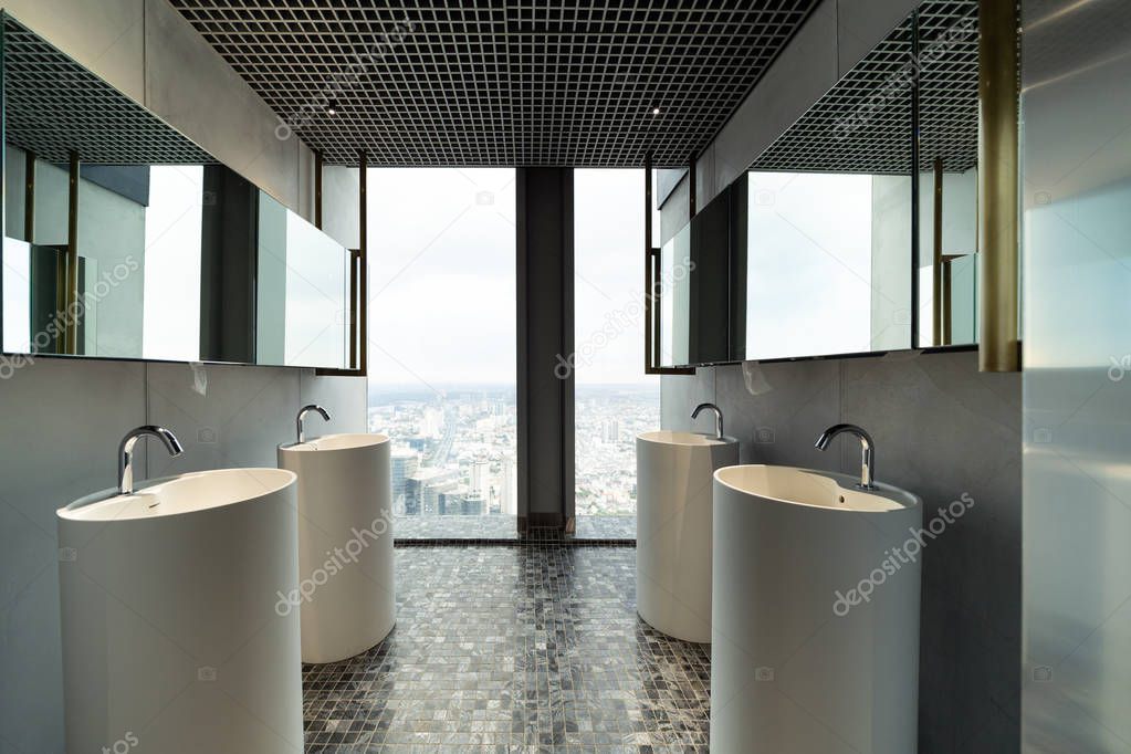 Row of modern white ceramic wash basin in public toilet with cityscape background, restroom in restaurant or hotel or shopping mall, interior decoration design