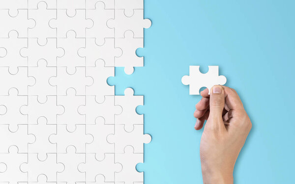 Рука кладет кусок белой головоломки. Текстура шаблона, разделенная в стратегии и решении концепции успешного партнерства командного бизнеса на синем фоне
.