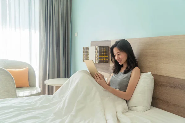 Felice donna asiatica sorridente e utilizzando un tablet sul letto in un moderno — Foto Stock