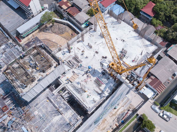 Aerial view of busy industrial construction site workers with cranes working. Top view of development high rise architecture building at noon.