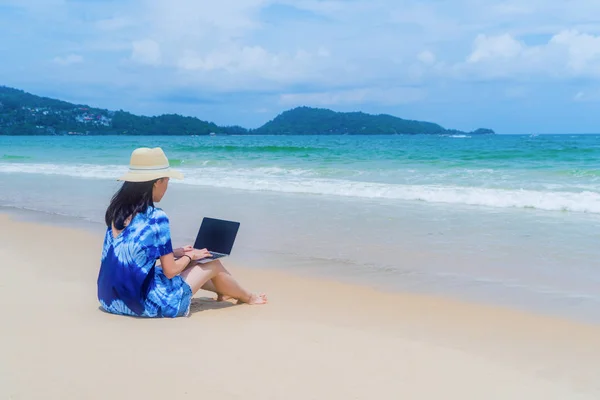 Mutlu Asyalı kadın tr sırasında plajda bir bilgisayar dizüstü bilgisayar kullanarak — Stok fotoğraf