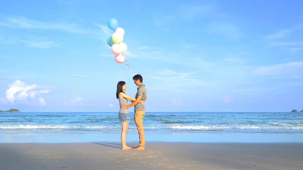 Feliz pareja asiática sosteniendo globos de colores en la playa durante — Foto de Stock