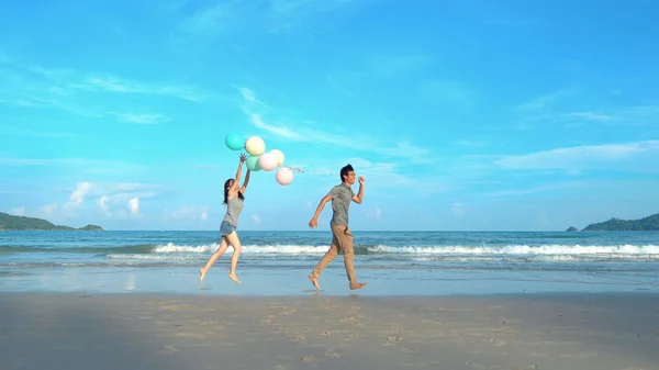 Boldog ázsiai házaspár gazdaság színes léggömbök a strandon alatt — Stock Fotó