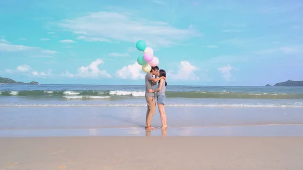 Happy Asian couple kissing, holding colorful balloons at the bea — Stock Photo, Image