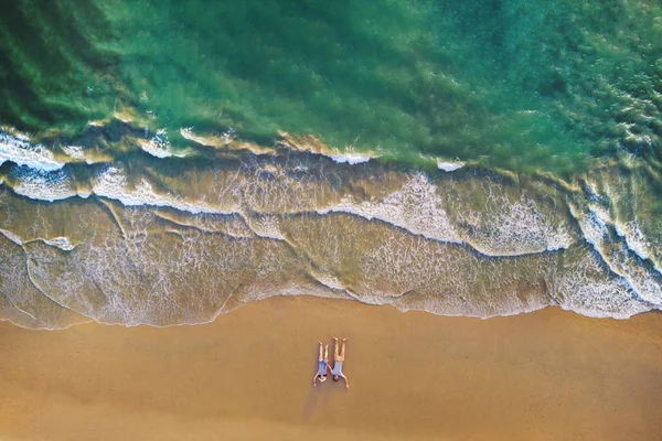 Luchtfoto van Aziatische paar liggend op het strand met golven rollen in — Stockfoto