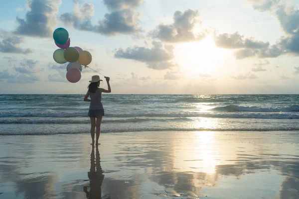 Happy Asian woman holding colorful balloons at the beach during — Stock Photo, Image