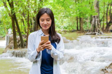 Mutlu Asyalı kadın sohbet etmek veya arkadaş aramak için mobil akıllı telefon kullanarak