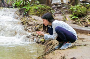 Mutlu Asyalı kadın tropikal şelaleden su içme 