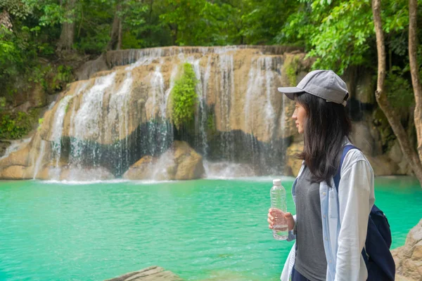 Heureuse femme asiatique buvant de l'eau d'une bouteille à la cascade en t — Photo