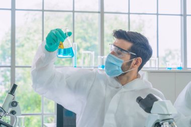 Mavi test tüpü üzerinde çalışan Asyalı bilim adamı laboratuvarda ya da laboratuvarda teknolojik tıp, kimya, sağlık, araştırma konsepti laboratuvarında covid-19 virüsü aşısı geliştirdi ve analiz etti. Deneysel bilim