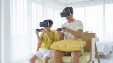 Baba ve oğul sanal gerçeklik gözlüğü takıyor, kulaklık takıyor ve teknoloji ve yenilik kavramında TV karşısında televizyon karşısında oyun oynuyor. Aile eğleniyor. Eğlence