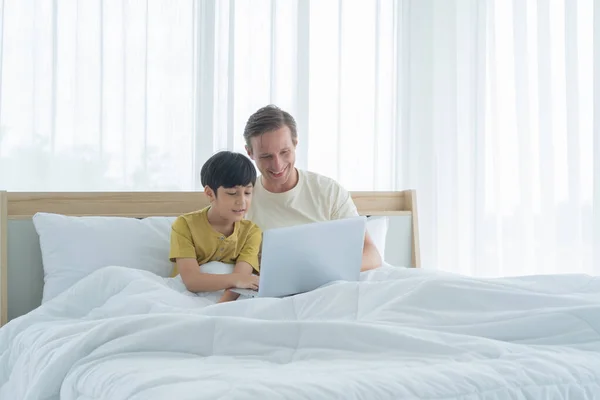 Happy smiling business blonde, man. Freelance working from home watching movie with his son with laptop computer notebook in quarantine. Family dad, children having fun together. Lifestyle.