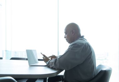 İş dünyasından yaşlı yaşlı siyahi bir adam, akıllı telefon ya da cep telefonu kullanan Afrikalı bir insan evdeki oturma odasında teknoloji aygıtı konseptinde. Yaşam tarzı insanları.