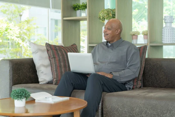 Smiling business senior old elderly Black American man, African person working from home on table with computer notebook laptop in quarantine in corona virus pandemic concept.