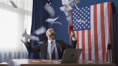 Zengin bir iş adamı, beyaz bir beyefendi, Amerikan ya da Amerikan bayrağı taşıyan beyaz bir adam finansal hesapta para tabancası ve bilgisayar dizüstü bilgisayarı ile yatırım konsepti kullanıyor..