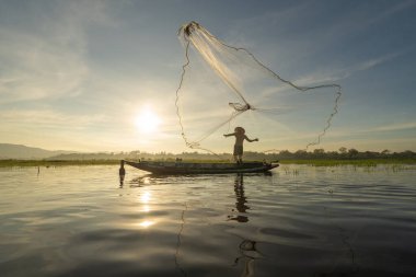 Siluet Balıkçısı, Tayland 'da Asya' da sabah saatlerinde, doğa gölünde ya da nehirde tatlı su balığı yakalamak için ağ atıyor ya da atıyordu. İnsanlar.