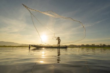 Siluet Balıkçısı, Tayland 'da Asya' da sabah saatlerinde, doğa gölünde ya da nehirde tatlı su balığı yakalamak için ağ atıyor ya da atıyordu. İnsanlar.