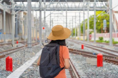 Asyalı bir kadın, bir turist, tren ya da tramvayla seyahat ediyor elektrik direkleri, kule ve kablolarla kentsel taşımacılık kentindeki terminal istasyonunda..