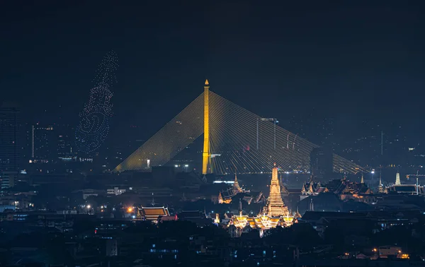 Drone show about The King rama 9, Bhumibol Adulyadej in memorial, at Rama 8 Bridge and Temple of Dawn or Wat Arun, Urban town city, Bangkok skyline. downtown area, Thailand at night.