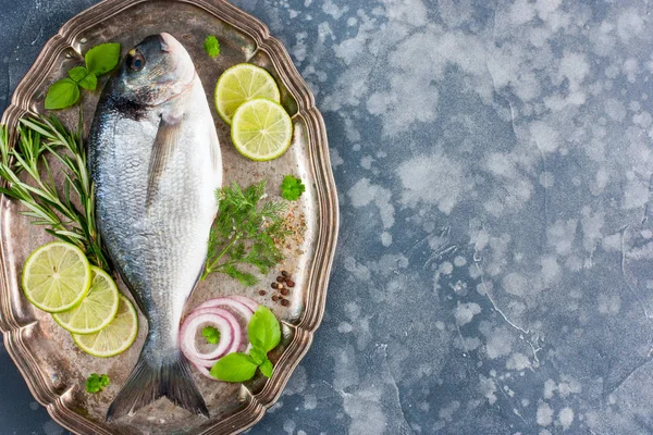 Fresh raw Dorado fish with fresh herbs (basil, parsley, dill, rosemary), spices (salt, pepper, dried herbs, onion), lime, top view, horizontal, copy space